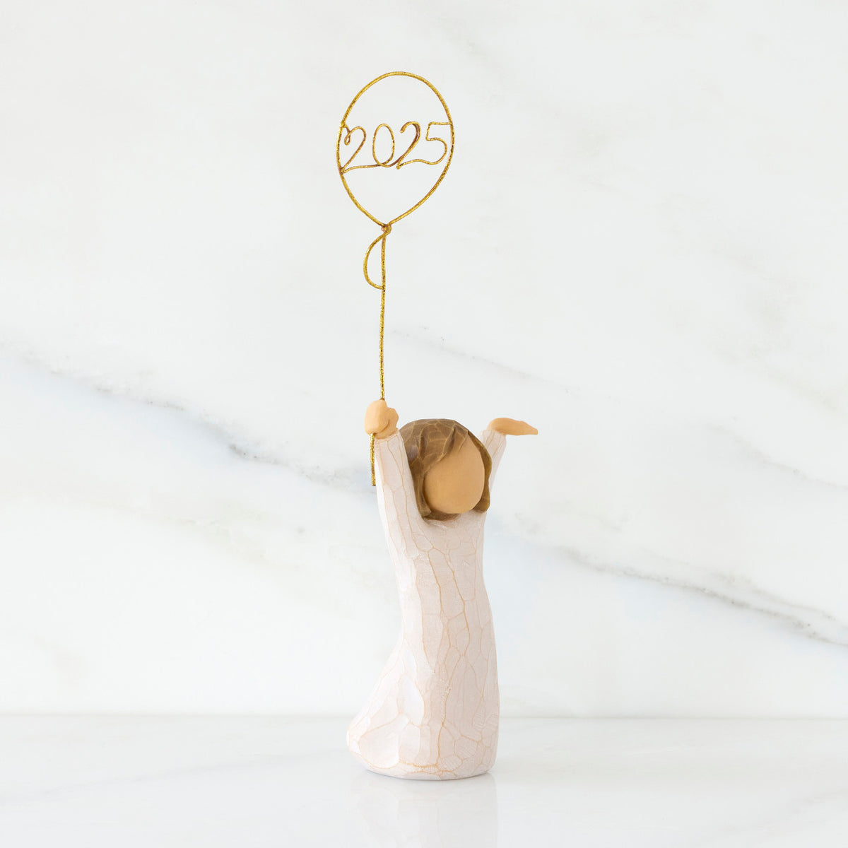 Facing right: standing figure in cream dress, arms raised, holding gold wire balloon with 2025 written in gold wire inside