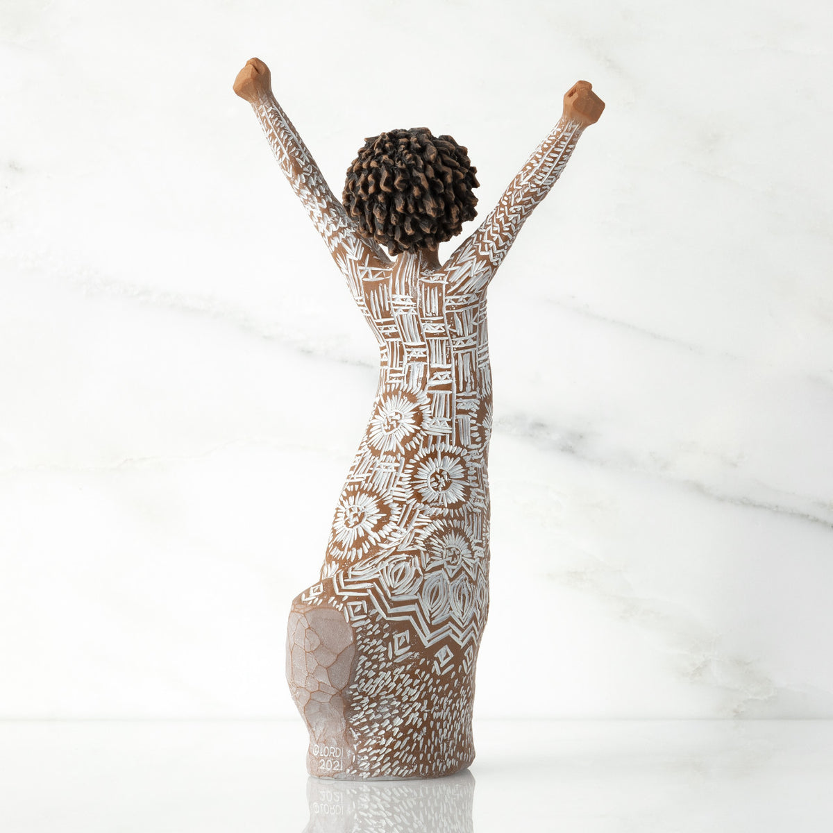 Right back of figure, with arms raised overhead, dress etched with African textile patterns