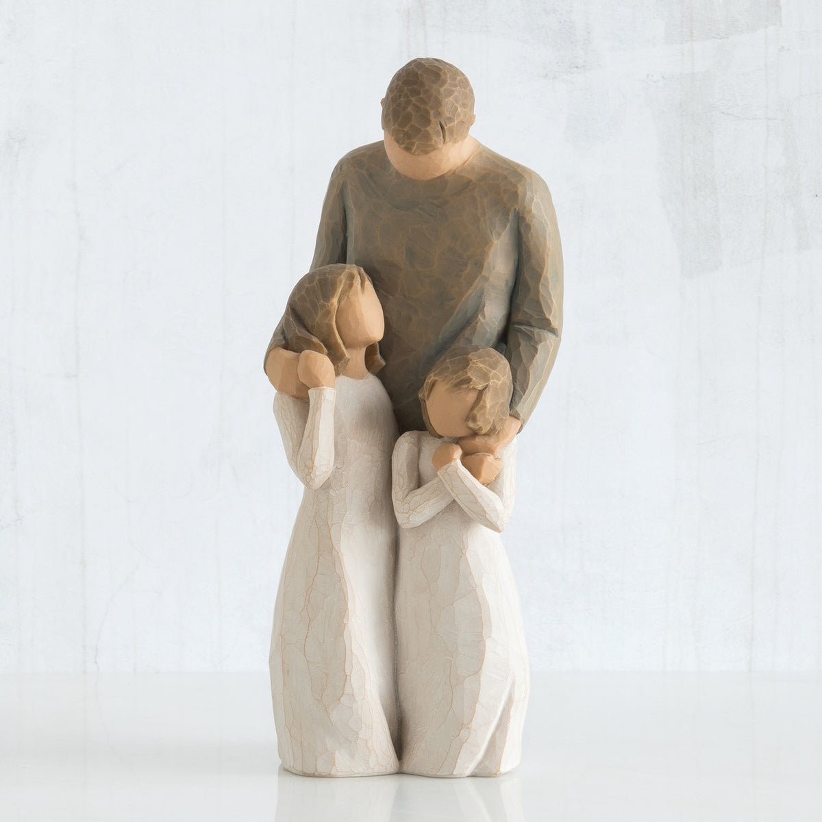 Man faceless figurine wearing brown shirt standing over two faceless girl figurines in white dresses