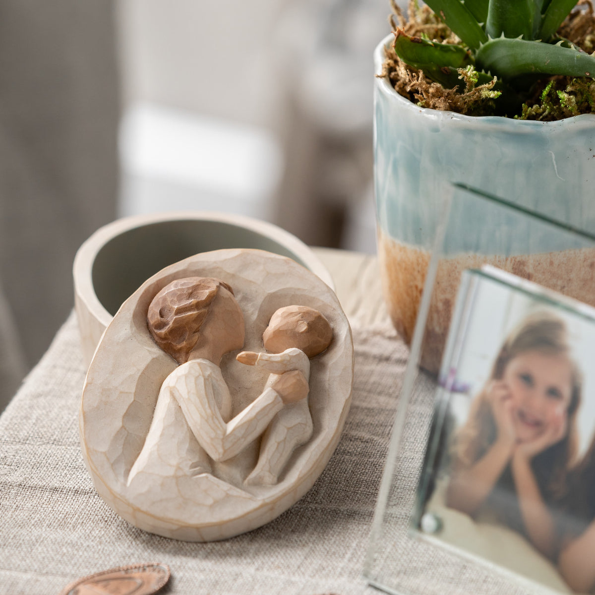 Willow Tree Grandmother Keepsake Box, 3.4" oval x 1.5" h hand-painted resin box with removable lid off to one side. Lid has bas-relief carving of older woman in cream dress, holding up baby, inside of box has sentiment
