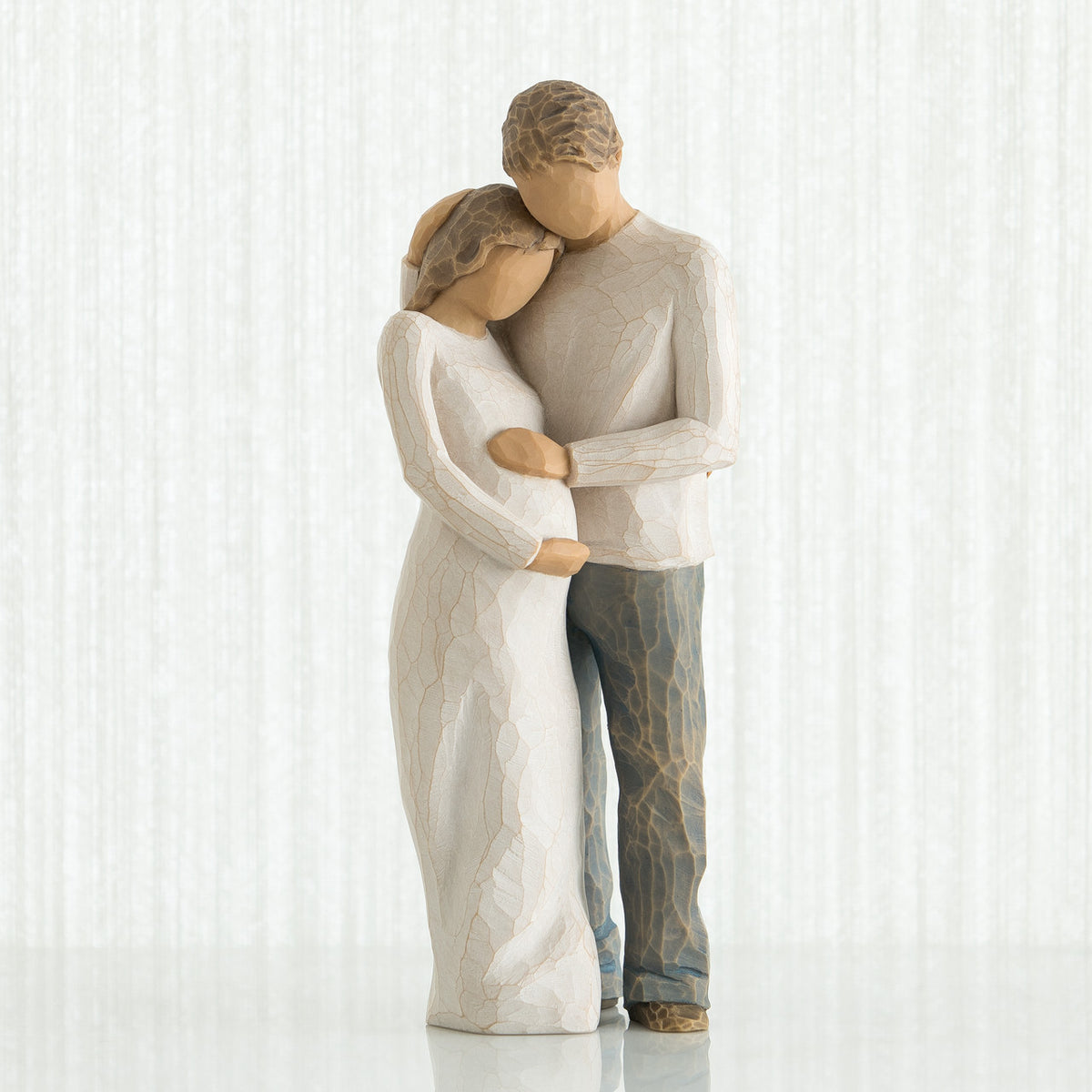 Man and woman faceless figurines - woman is wearing white dress and man is wearing white shirt and blue jeans holding woman's stomach