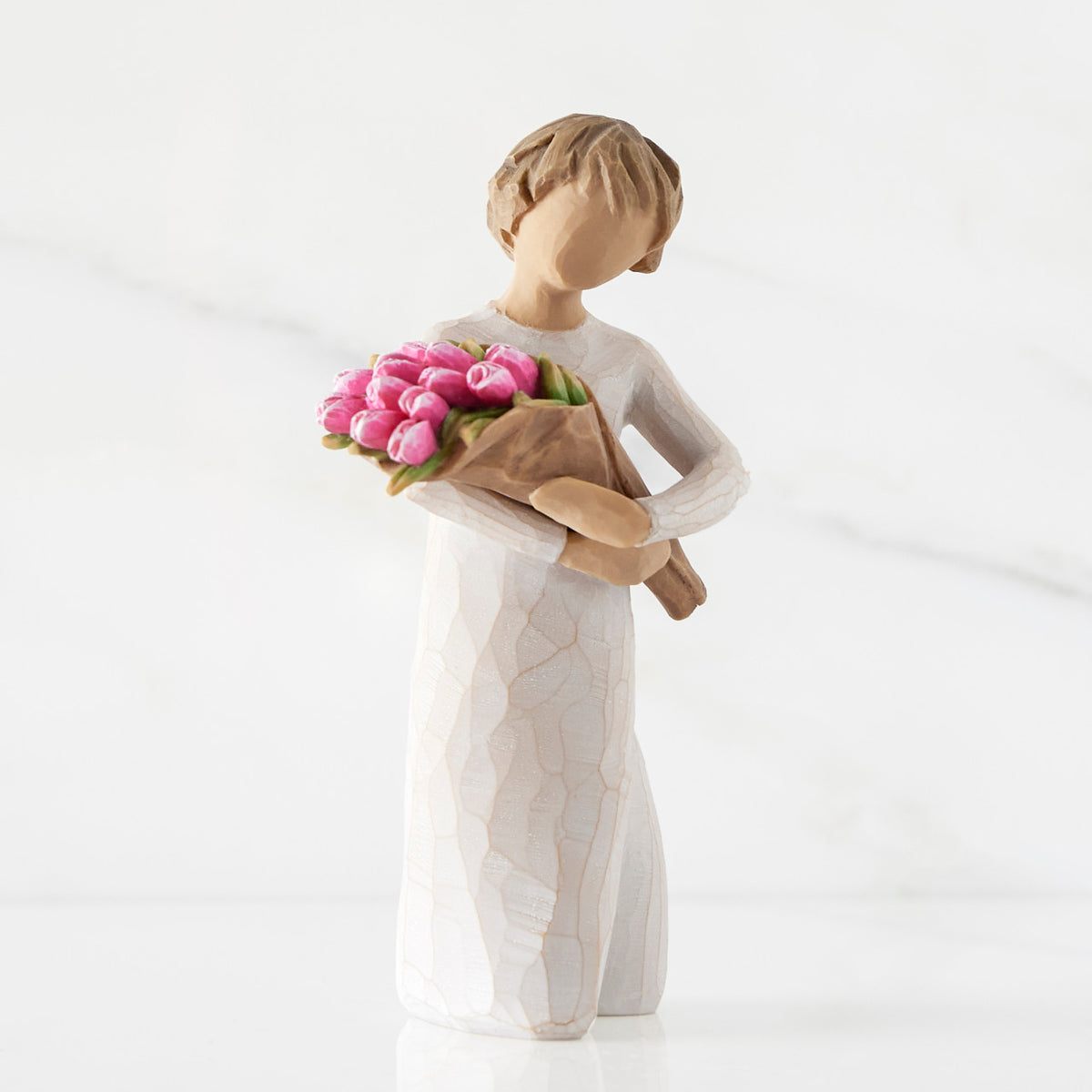 Right side of standing figure in cream dress holding bouquet of pink tulips