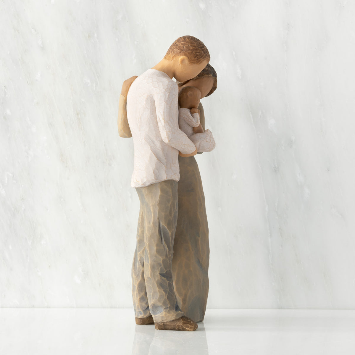 Right view of standing couple, woman has darker skin and hair; man has lighter skin and hair, holding a baby between them.