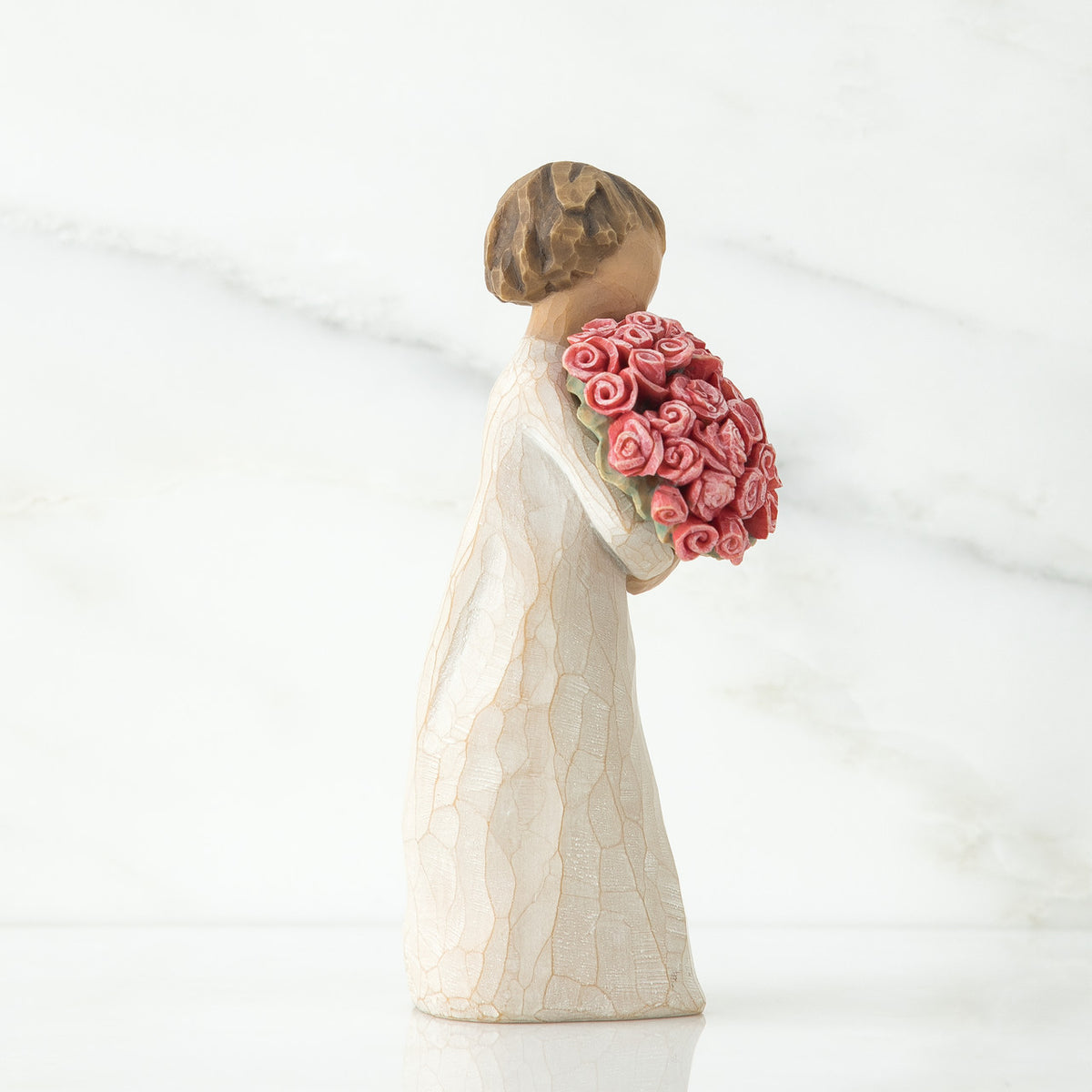 Side view of young brunette girl figurine in white dress standing holding pink roses