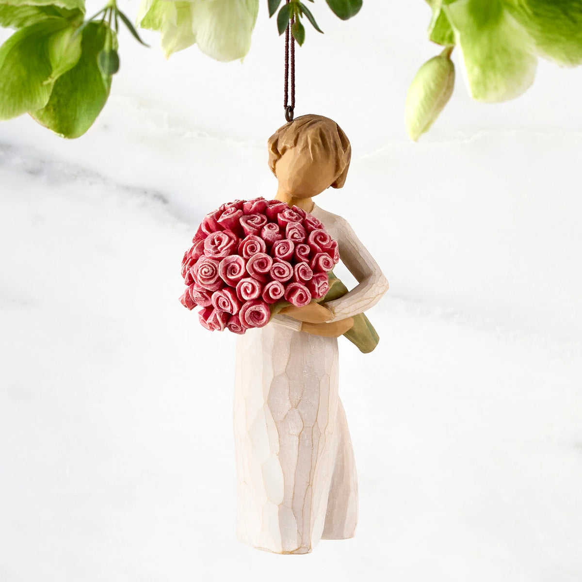 Front view of female figure with short brown hair holding large bouquet of pink roses, ornament loop affixed to top of head