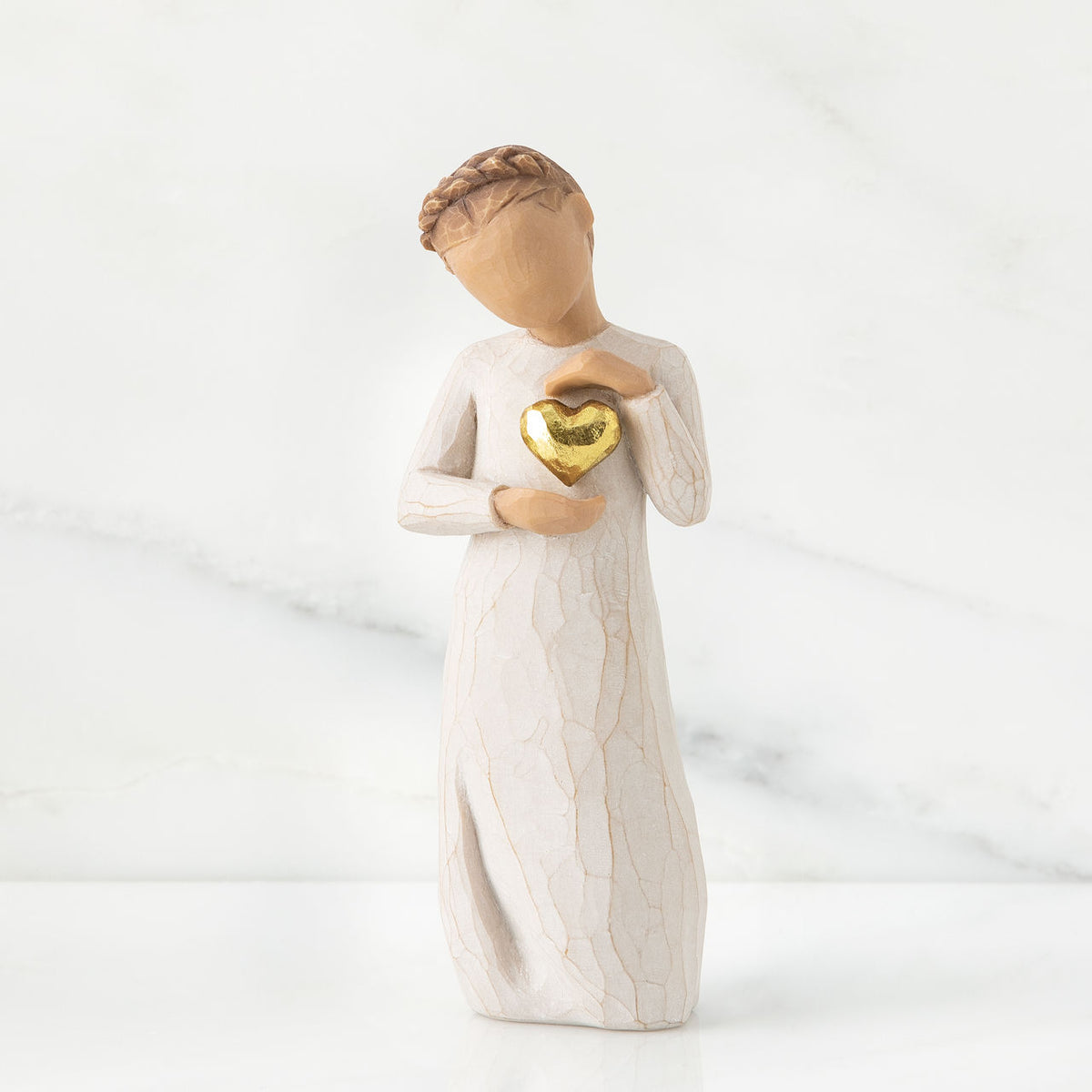 Small girl figurine wearing white dress holding up gold heart pendant