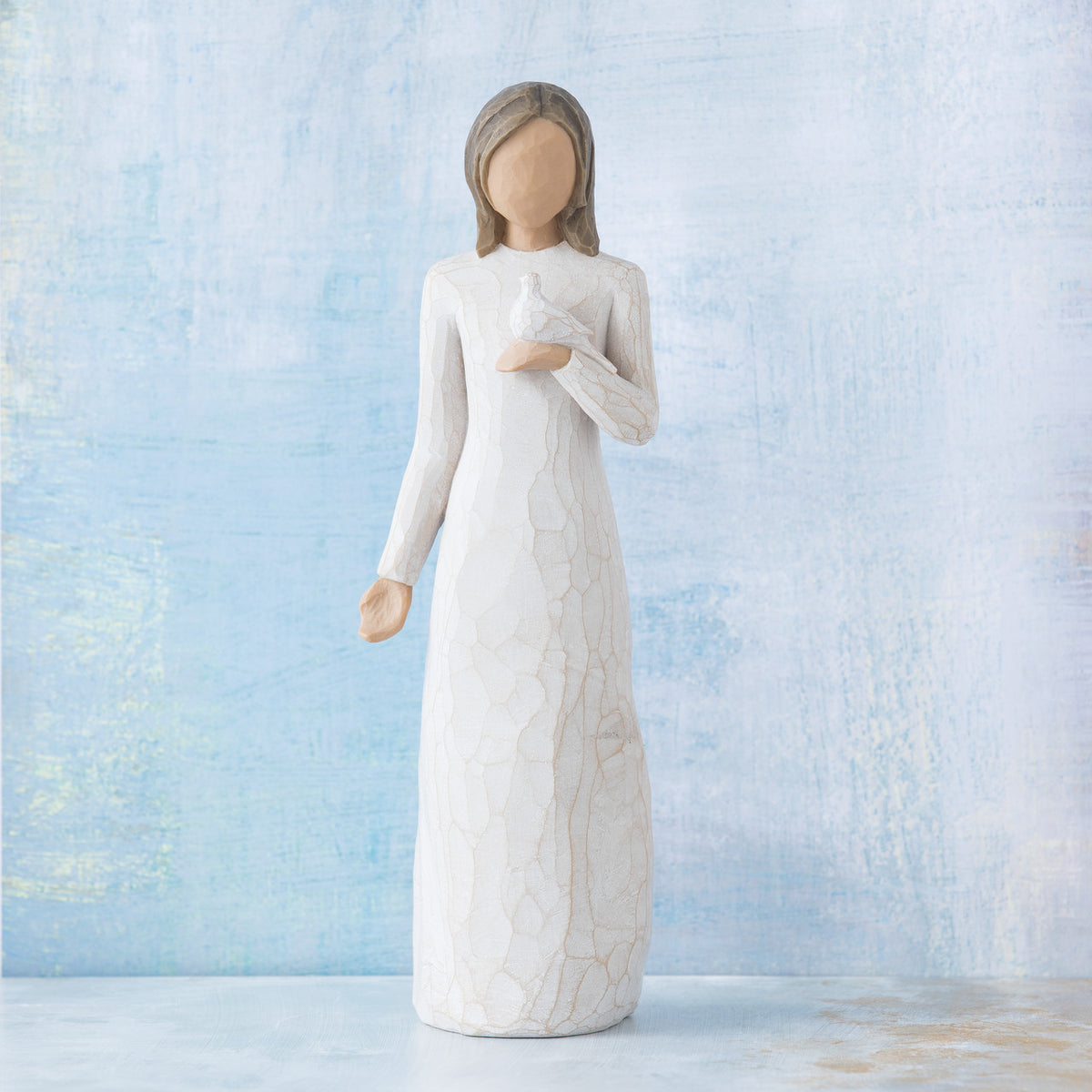 Willow Tree With sympathy, 9”h hand-painted standing resin figure in cream dress, holding white dove on hand, in front of pale blue painting