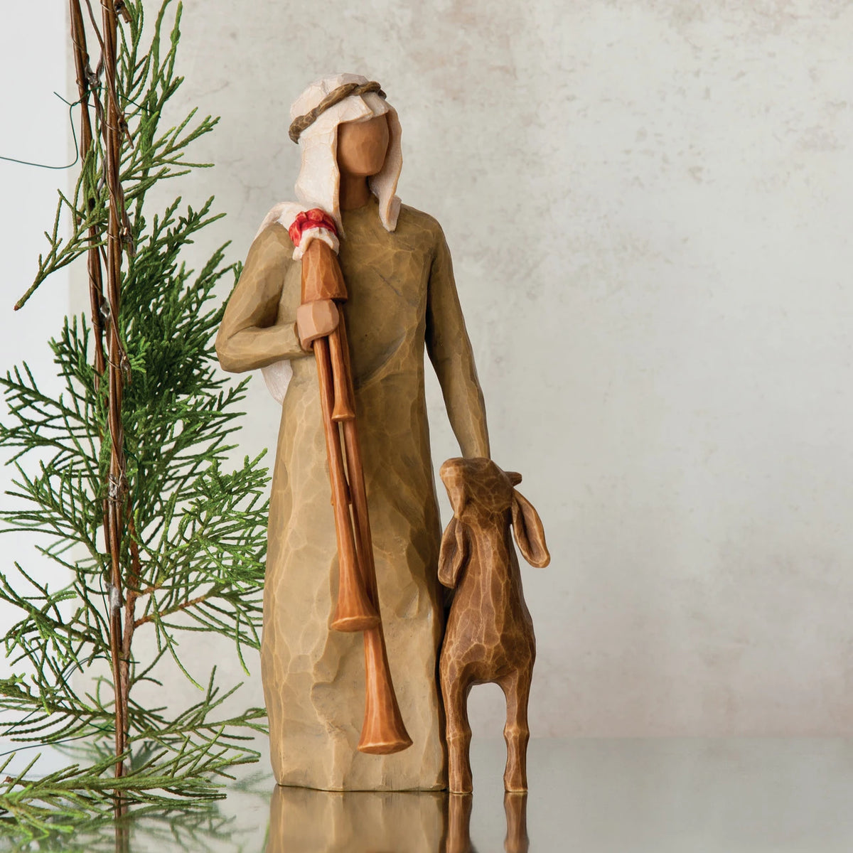 Wiseman figurine in tan dress next to golden lamb figurine with green tree in the background