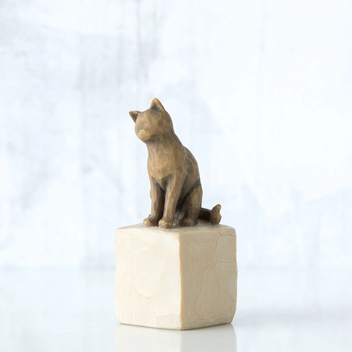Golden and grey cat figurine sitting on white rock