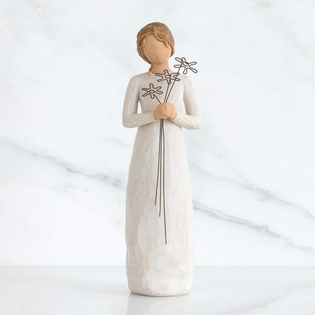 Front view of girl with brown hair in a bun holding three flowers with long stems up to her chest with both hands
