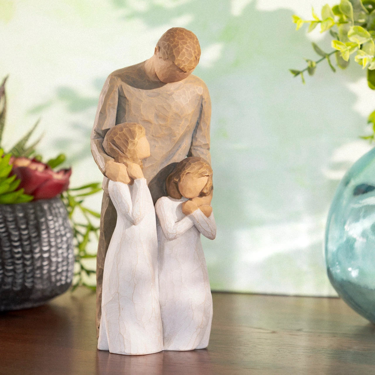 Willow Tree My Girls, 8"h hand-painted standing resin figure of father with arms around two young girls, all in neutral clothing, on shelf in dappled light