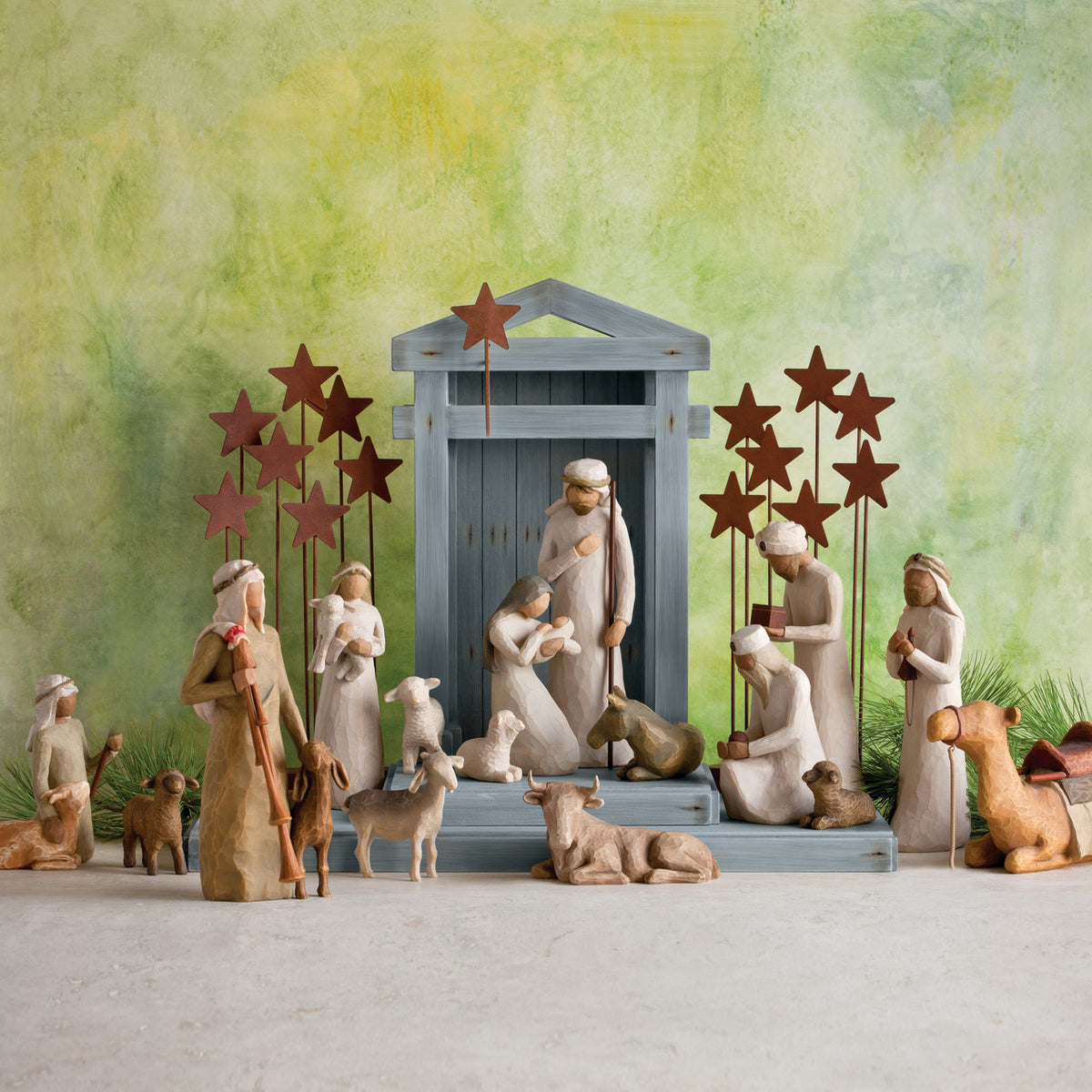 Far front view of grey barn with wiseman figurines, golden cows, and white sheep figurines around the barn - green background