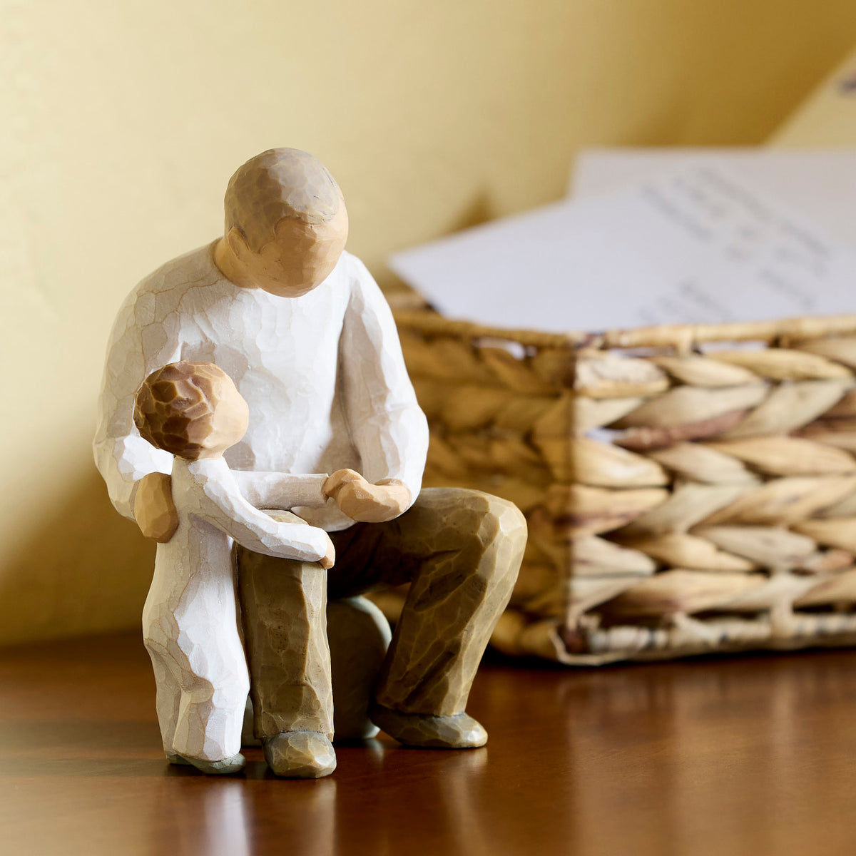 Willow Tree Grandfather, 6”h hand-painted resin figure of seated older man with toddler by his side, both dressed in neutral colors, on wooden table with basket
