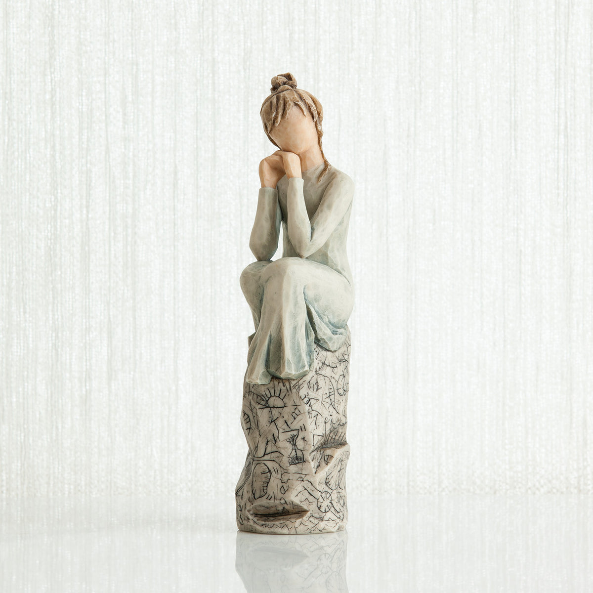 Woman figurine with brown hair in a bun and in white/blue dress sitting on grey printed rock