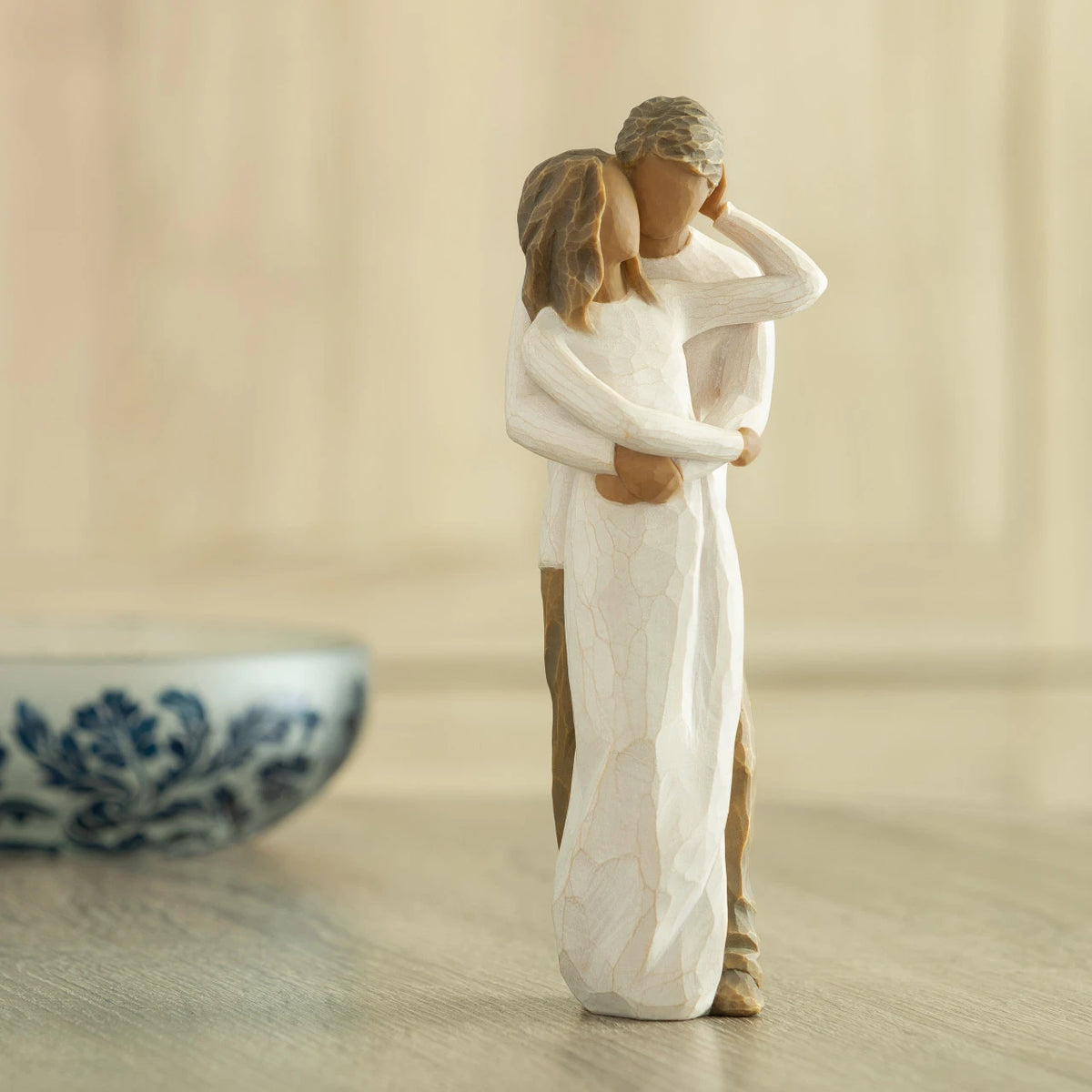 Front view of couple, standing with arms around each other. Woman and man have darker skin tones and hair color. Decorative bowl in background.