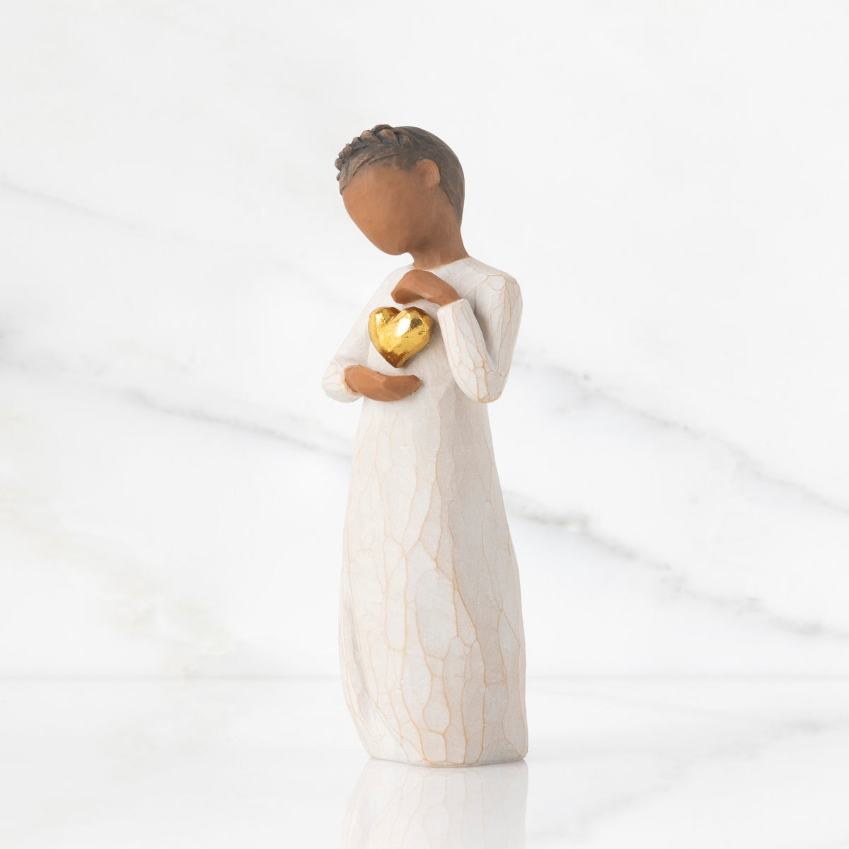 Left view: standing figure in cream dress with darker skin and dark hair braid, arms and hands framing gold leaf heart on chest