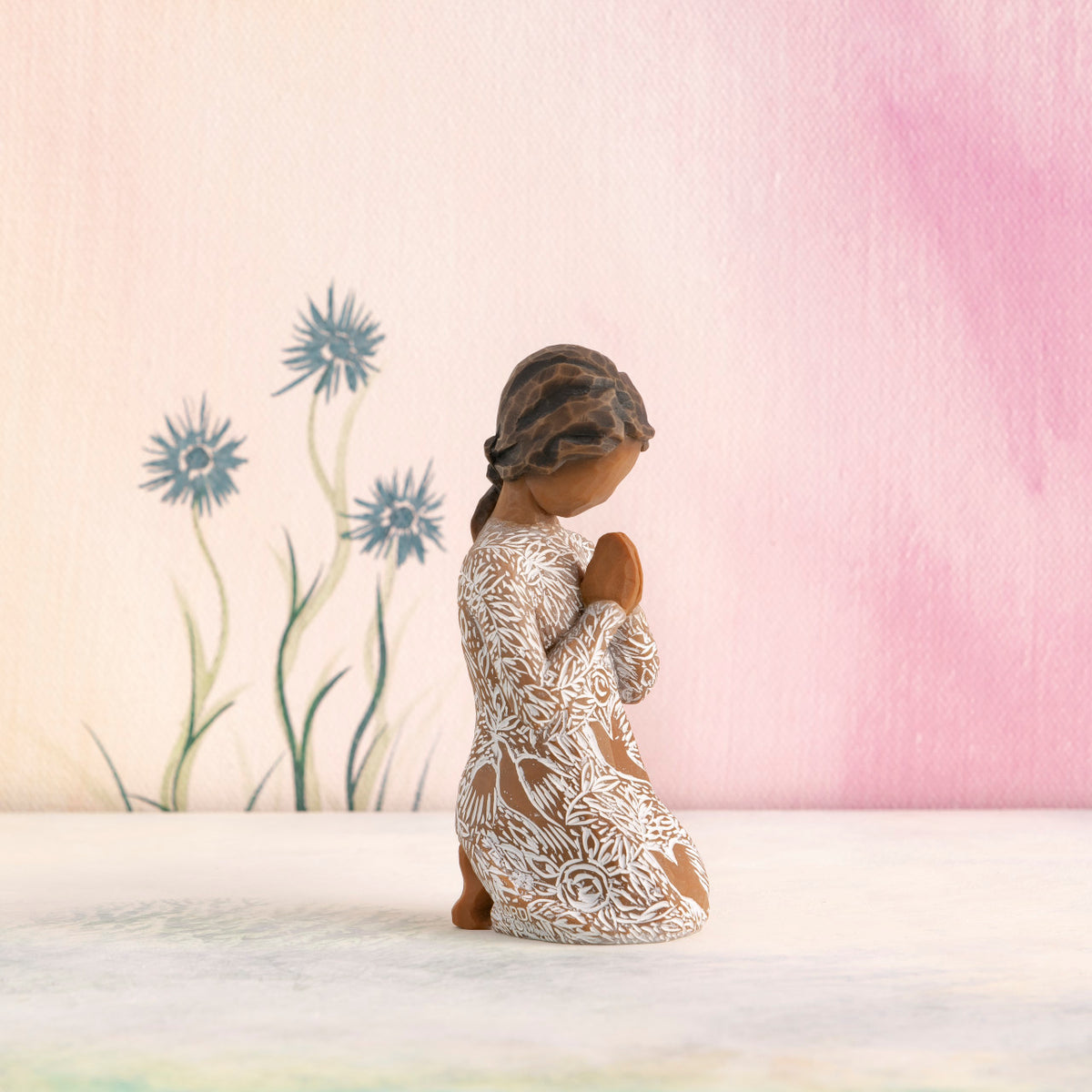 Willow Tree Prayer of Peace, 4”h hand-painted kneeling figure with darker skin and hair, in cream dress carved with nature imagery, in prayer/meditation pose, in front of pale pink painting