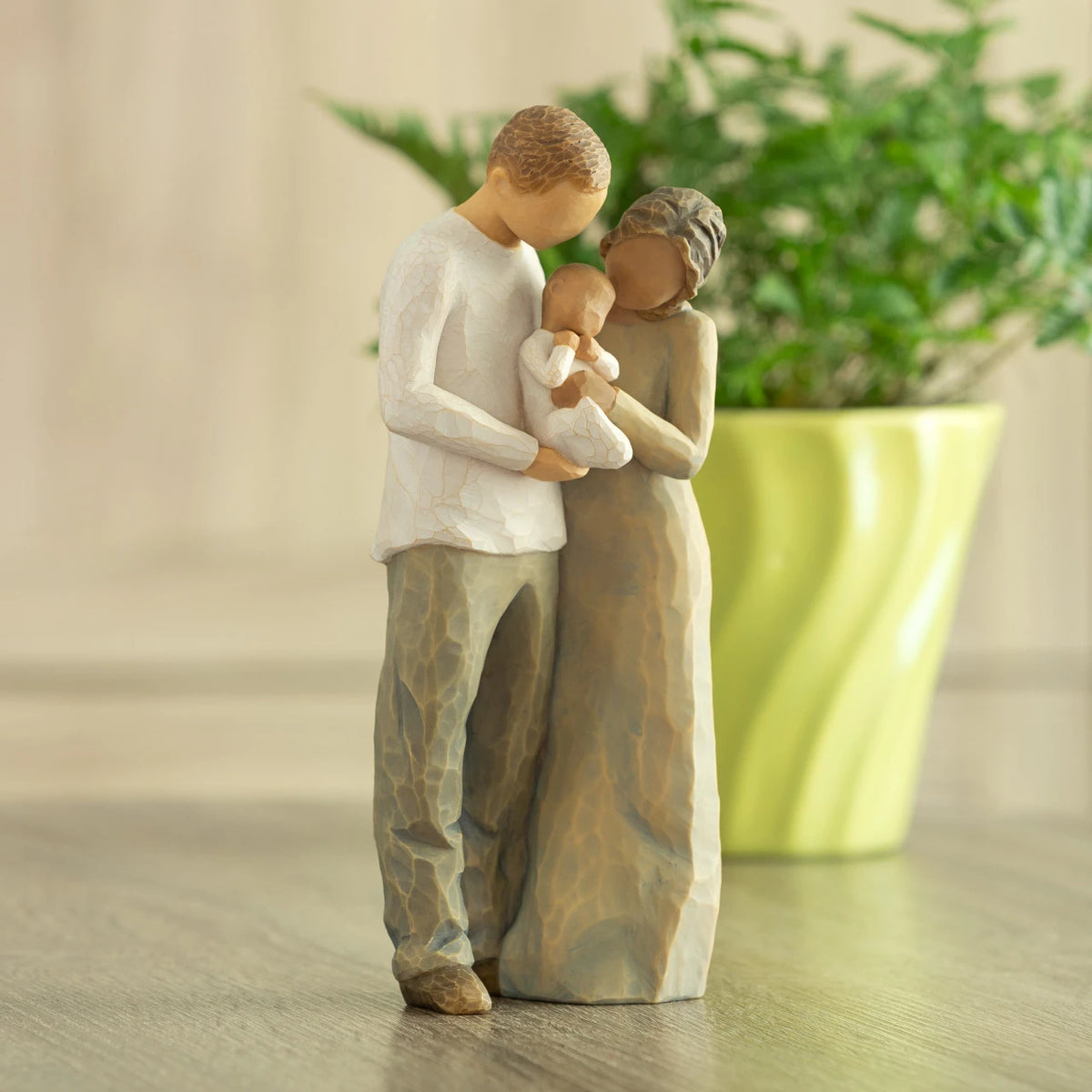 Front view of standing couple, woman has darker skin and hair; man has lighter skin and hair, holding a baby between them. Potted plant in background.