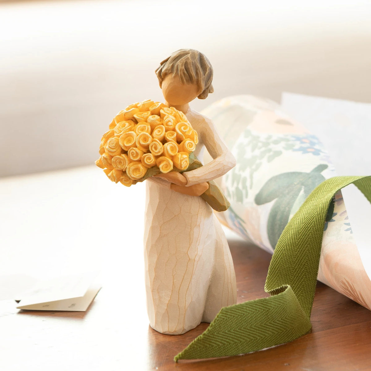 Willow Tree Good Cheer, 5.5" hand-painted standing resin figure in cream dress, holding bouquet of yellow roses, on table near window