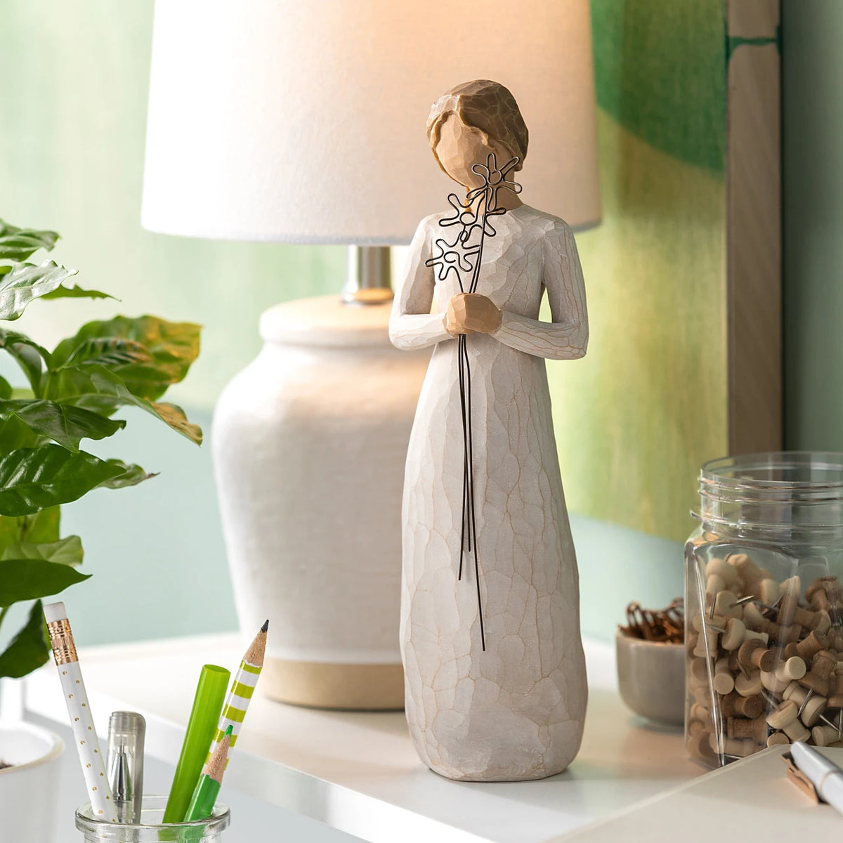 Willow Tree Grateful, 9”h hand-painted standing resin figure in cream dress, holding three wire flowers with long stems, on shelf with white lamp