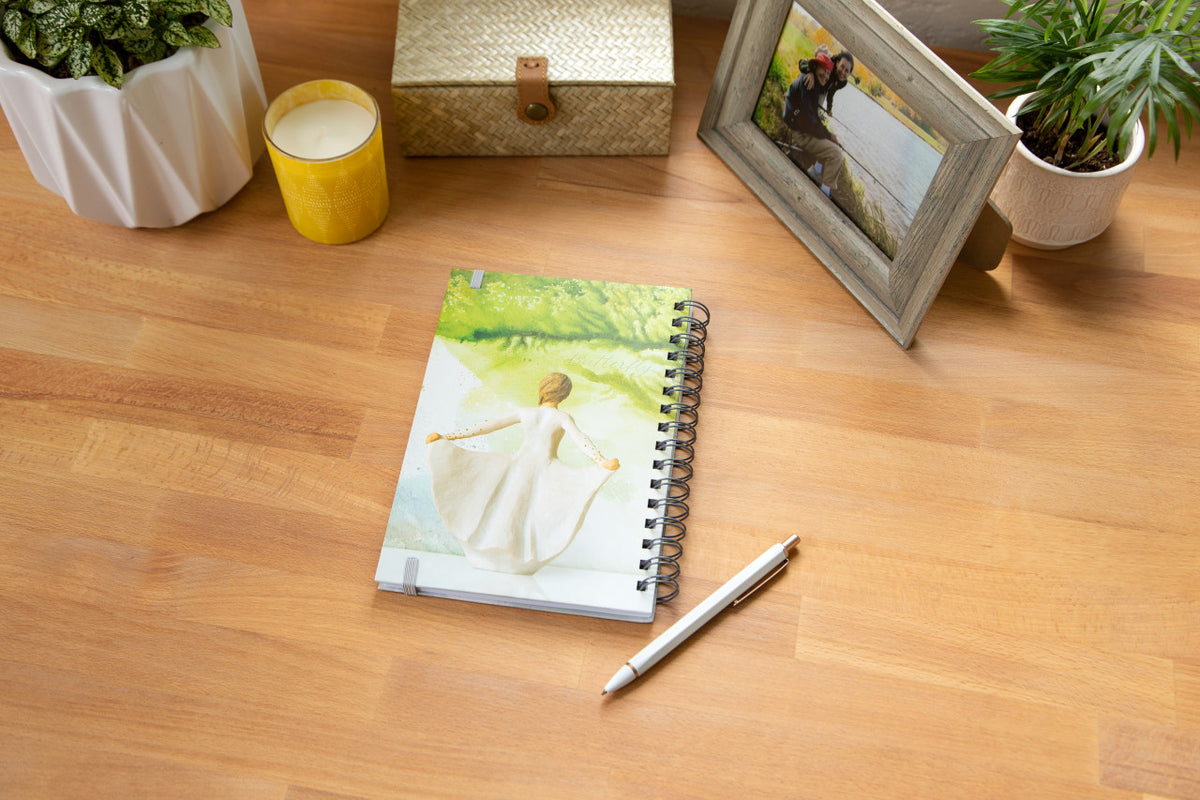 Willow Tree Butterfly Notebook, 6.5"w x 8.5"h, hard-cover, spiral-bound, 240 lined pages, back cover features back of Butterfly figure on background of light green painting, closed on desk