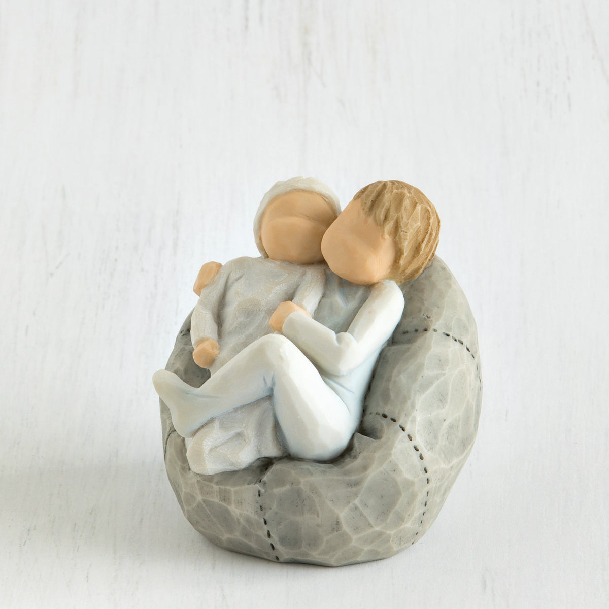 Two faceless baby figurines hugging one another on grey bean bag figurine