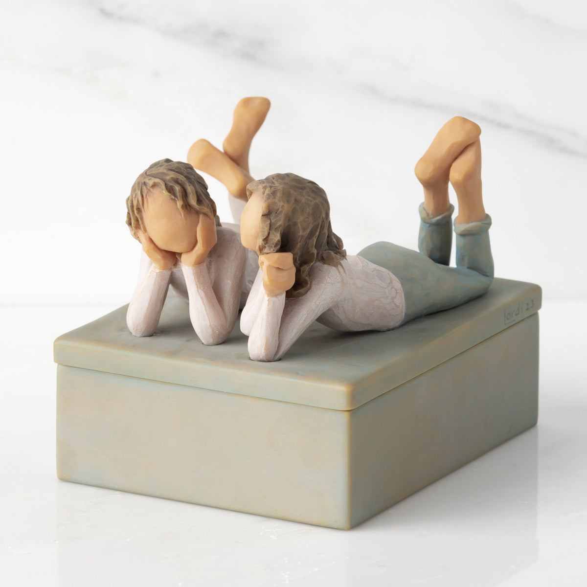 Left view of closed rectangular blue-gray resin box, sculpture of two girls affixed to lid