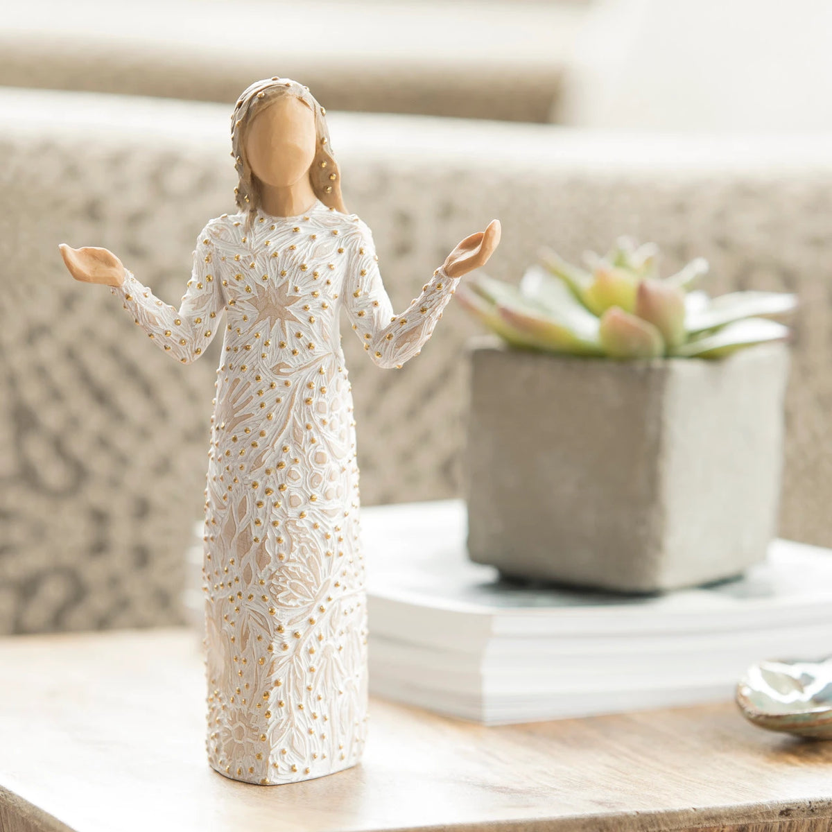 Willow Tree Everyday Blessings, 6.5”h hand-painted standing resin figure with bent elbows and arms raised, cream dress carved with nature symbols and gold-leaf dots, on living room table