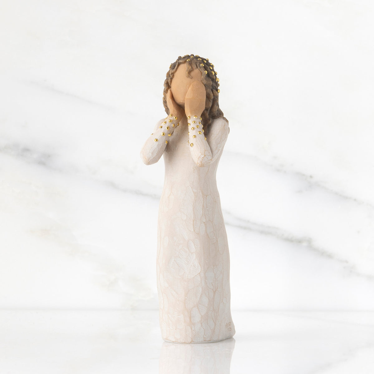 Front view: Standing figure in cream dress, both hands up to face, gold leaf dots on sleeves and throughout hair as a halo